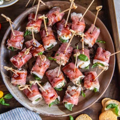 A platter filled with prosciutto wrapped mozzarella next to a bowl of marinated mozzarella balls.