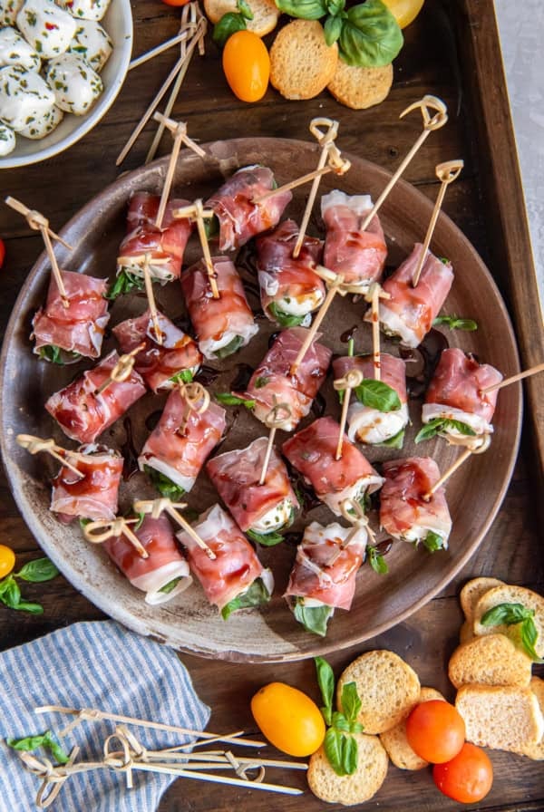 A platter filled with prosciutto wrapped mozzarella next to a bowl of marinated mozzarella balls.