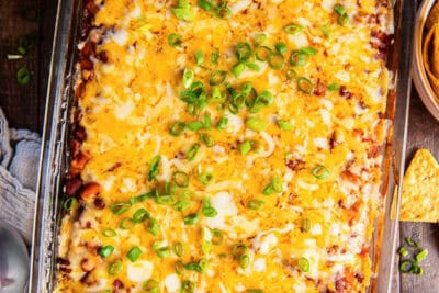 Chili cornbread casserole topped with green onions on a brown board next to a bowl of sour cream and tortilla chips.