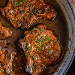Four braised pork chops with fresh thyme in a pan.