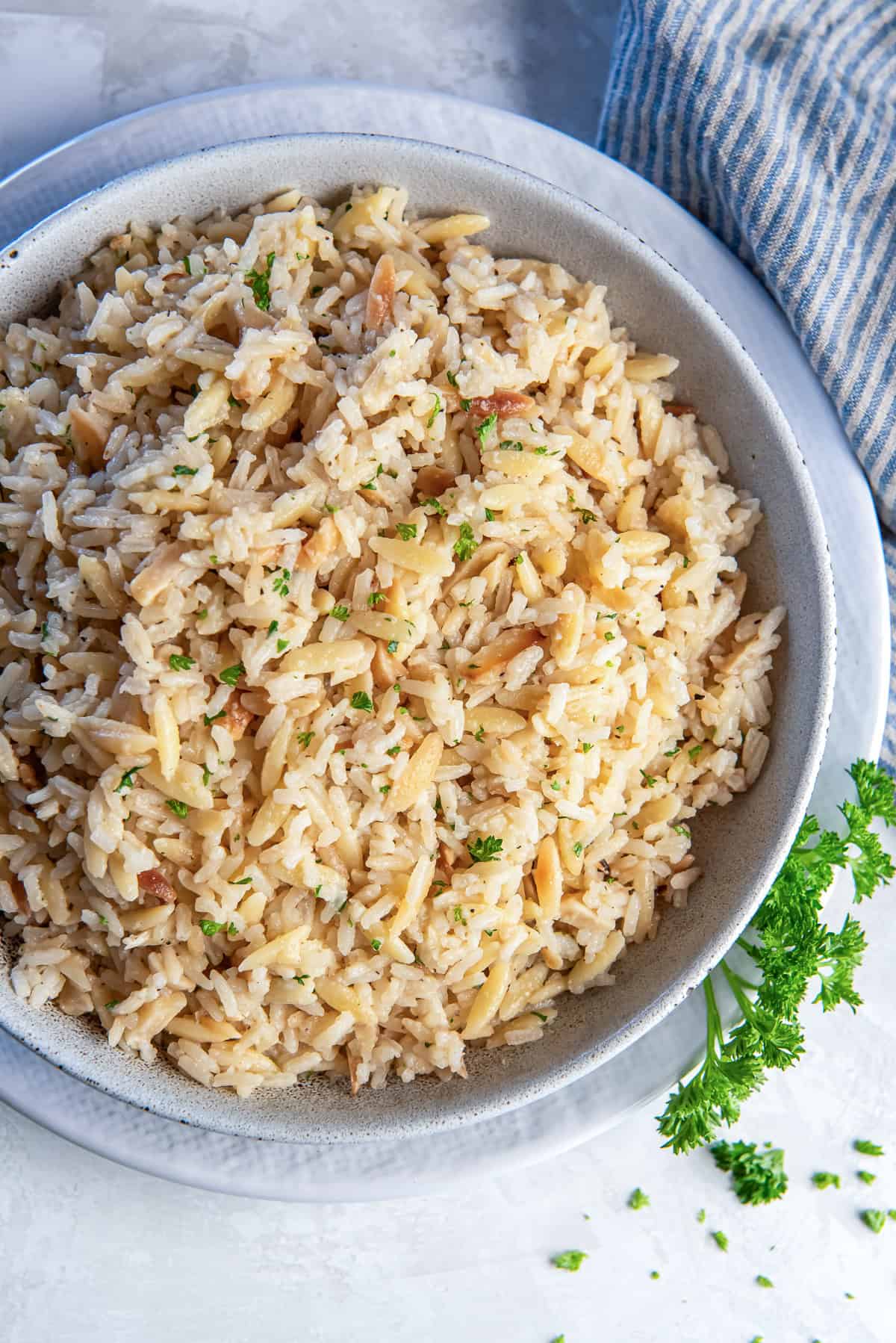 Almond rice pilaf in a white bowl resting on a plate with a sprig of parsley.