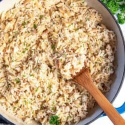 A wooden spoon resting in a pan full of almond rice pilaf.