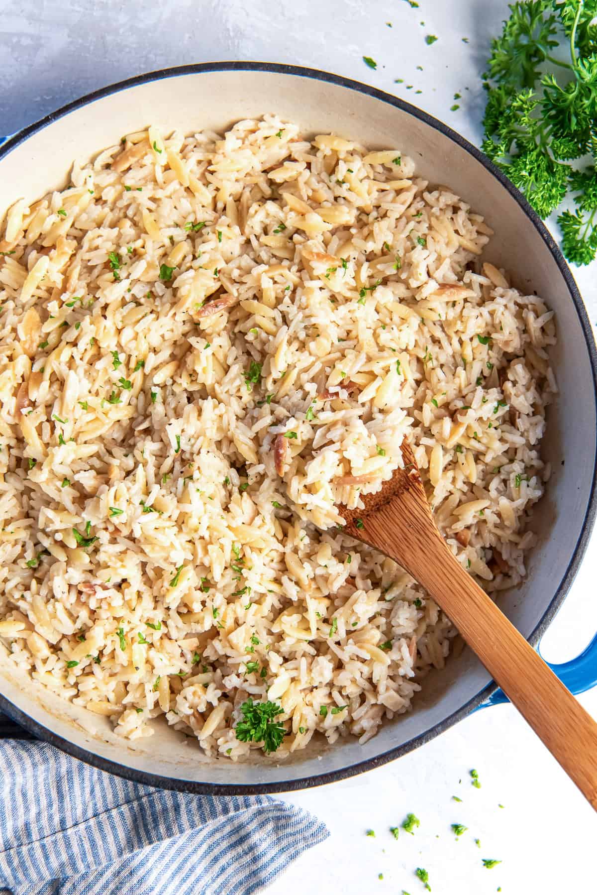 A wooden spoon resting in a pan full of almond rice pilaf.