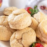 British scones piled on a white platter with a couple of fresh strawberries.
