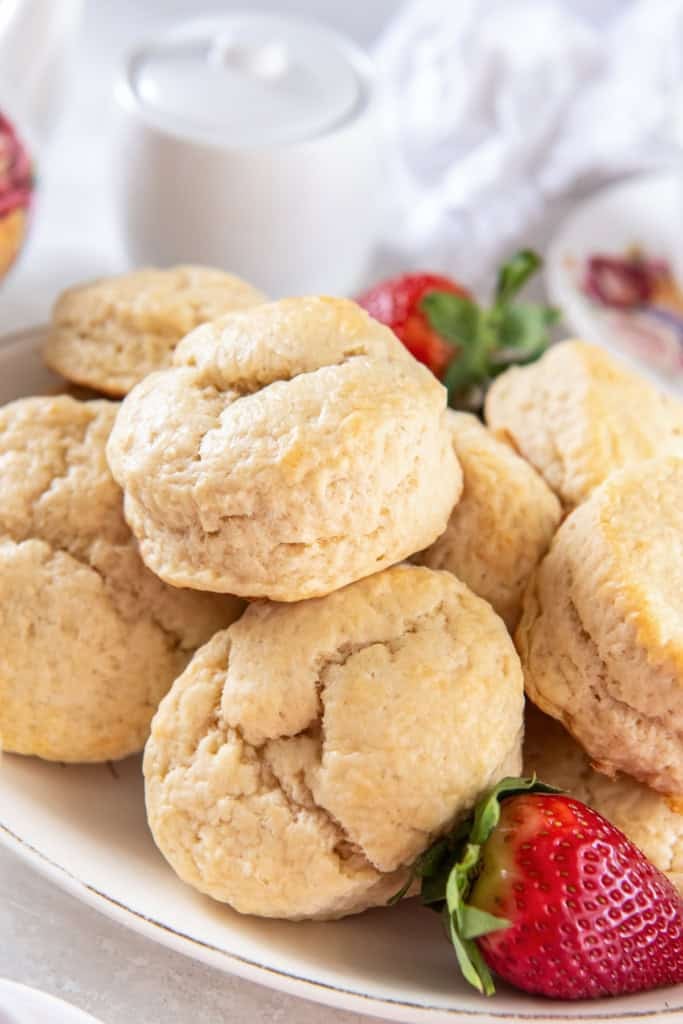 British scones piled on a white platter with a couple of fresh strawberries.