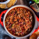 A pot of beef chili with bell peppers and mushrooms next to a bottle of Guinness.