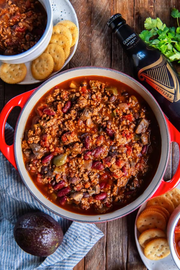 A pot of beef chili with bell peppers and mushrooms next to a bottle of Guinness.