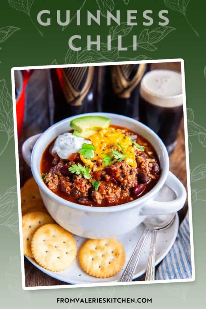 A bowl of Guinness chili with cheese and sour cream on a plate with crackers.