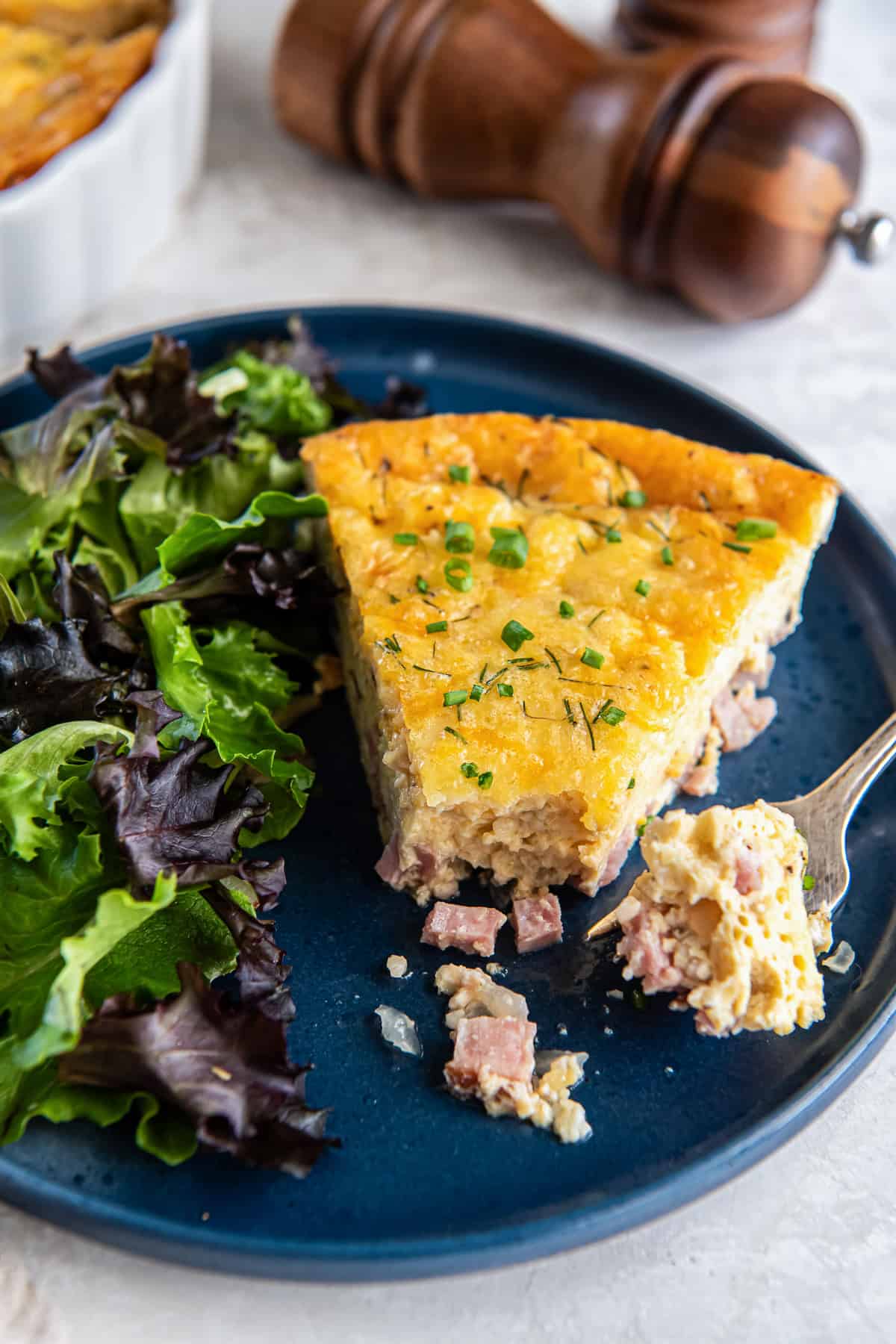 A fork with a bite of quiche resting on a blue plate.