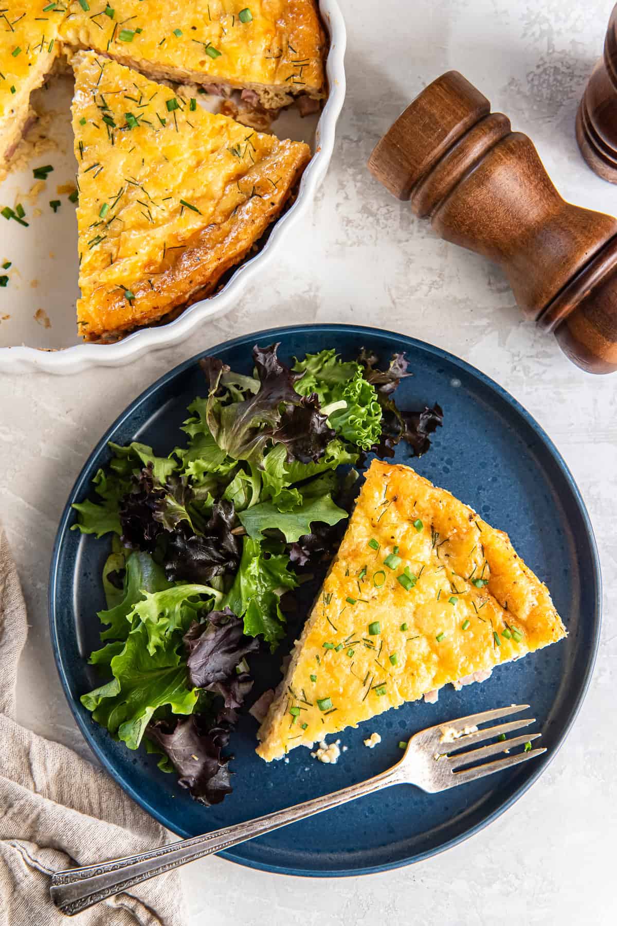 A fork resting on a blue plate with a slice of quiche and green salad.