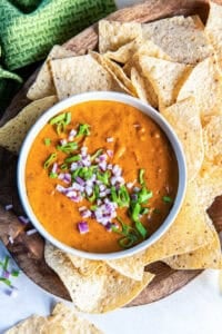 A bowl of chili cheese dip on a platter with tortilla chips.