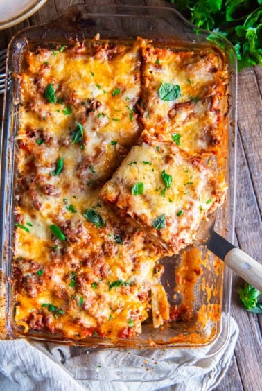 A spatula lifting a slice of lasagna from a baking pan.