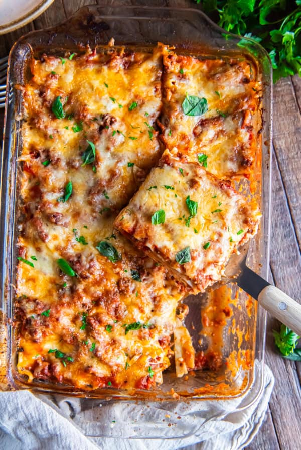 A spatula lifting a slice of lasagna from a baking pan.