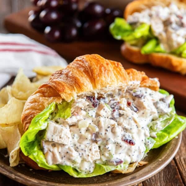 Cranberry chicken salad on a croissant wth lettuce on a wooden plate.