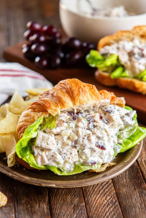 Cranberry chicken salad on a croissant wth lettuce on a wooden plate.