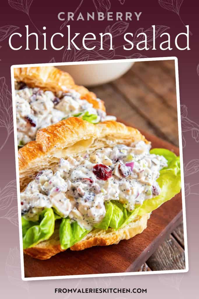 A croissant filled with cranberry chicken salad and lettuce on a wood cutting board with text overlay.