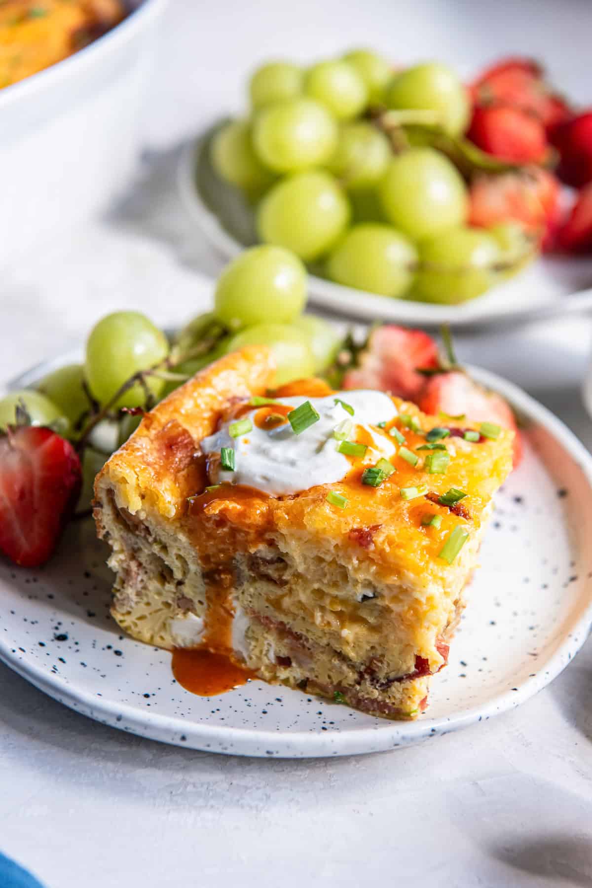 A slice of crustless quiche casserole on a white plate with grapes and strawberries.