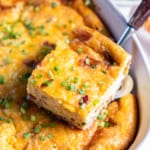 A spatula lifting a slice of quiche casserole from a white baking dish.