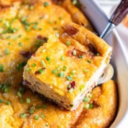A spatula lifting a slice of quiche casserole from a white baking dish.