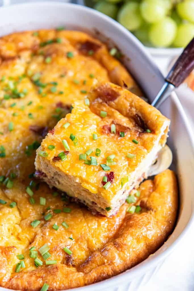A spatula lifting a slice of quiche casserole from a white baking dish.
