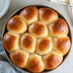 Dinner rolls in a round metal cake pan next to a butter dish.