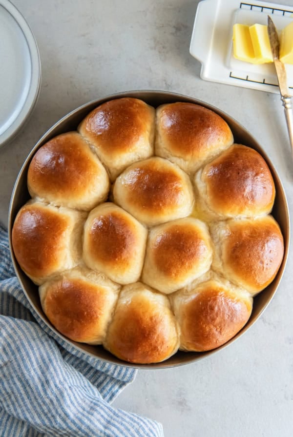 Dinner rolls in a round metal cake pan next to a butter dish.