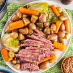 Sliced corned beef on a platter with cabbage, carrots, and potatoes, on a dinner table.