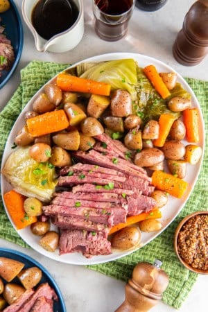 Sliced corned beef on a platter with cabbage, carrots, and potatoes, on a dinner table.