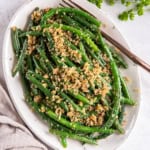 Italian green beans topped with Parmesan and breadcrumbs on a white serving plate.