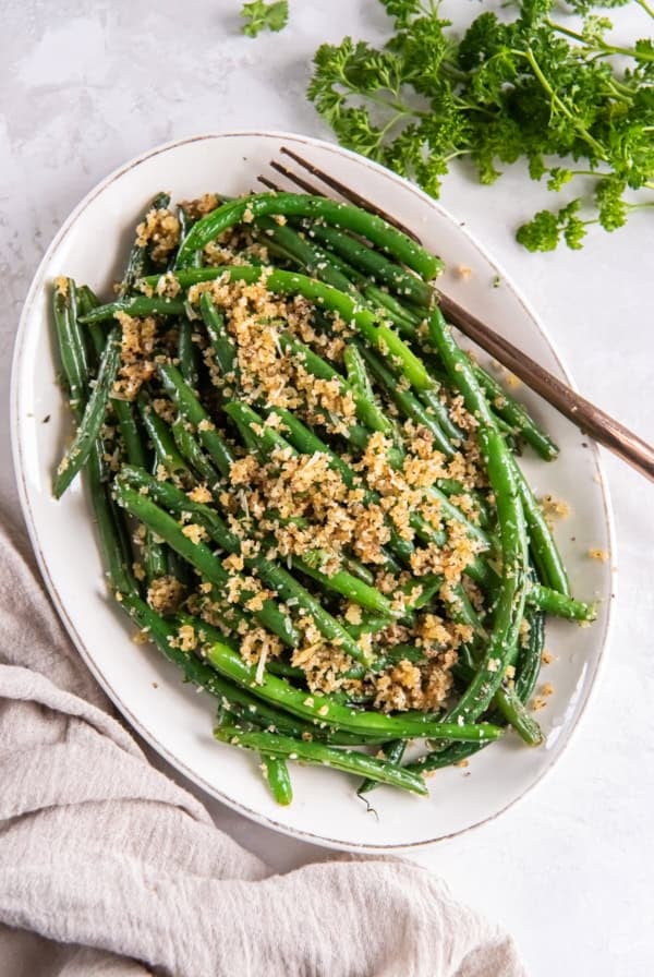 Italian green beans topped with Parmesan and breadcrumbs on a white serving plate.