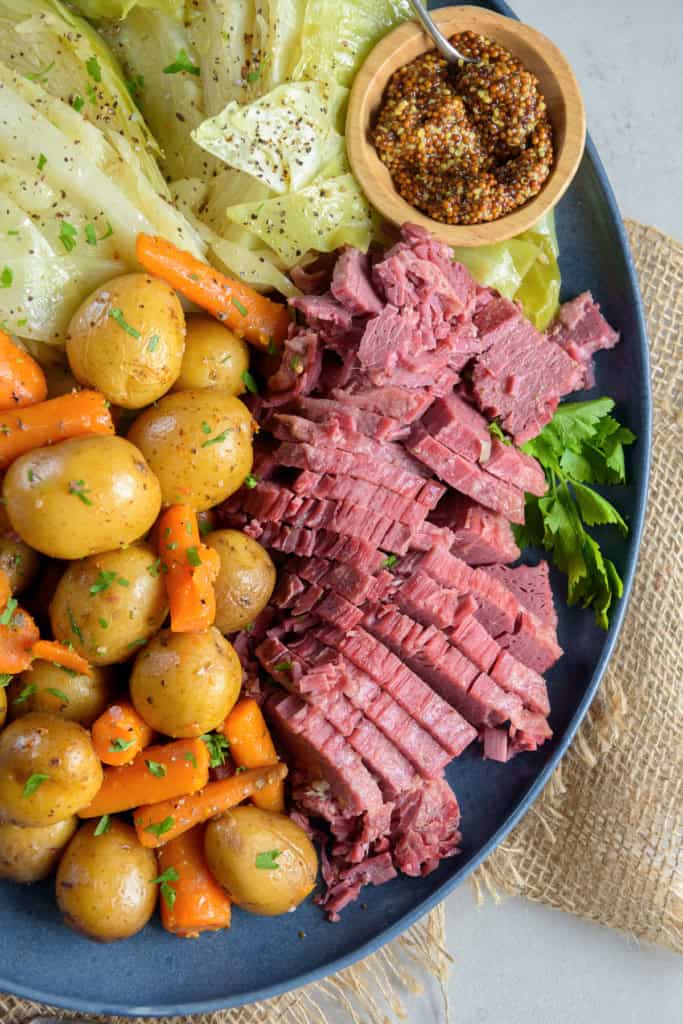 Sliced corned beef on a blue platter with carrots, potatoes, and cabbage.