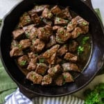 Steak bites garnished with parsley in a cast iron skillet.