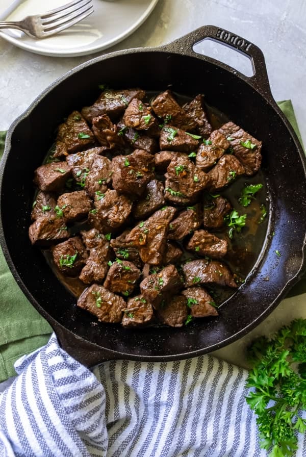 Steak bites garnished with parsley in a cast iron skillet.