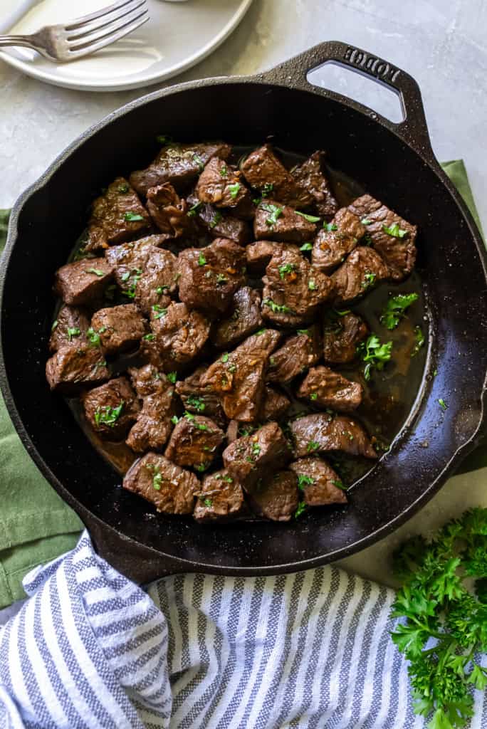 Steak bites garnished with parsley in a cast iron skillet.