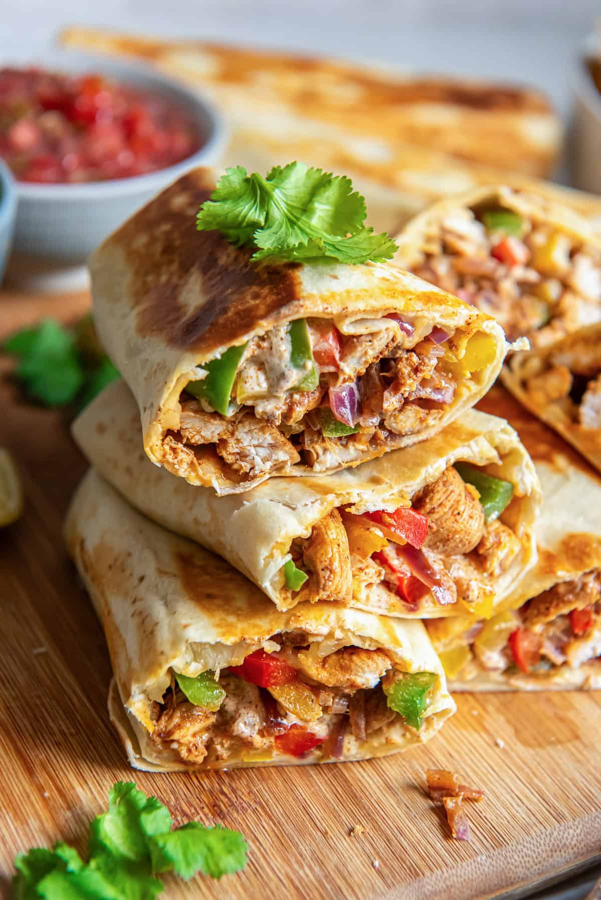 A stack of chicken fajita wraps in front of a bowl of salsa.