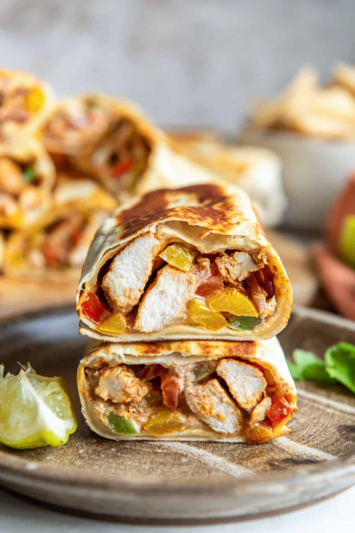 A chicken fajita wrap sliced in half and stacked on a plate.