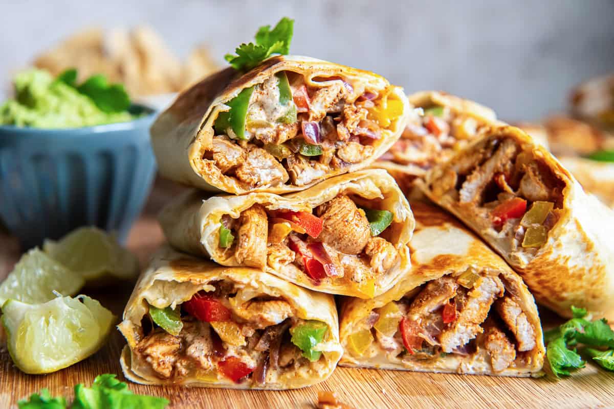 Chicken fajita wraps sliced in haf and stacked on a cutting board.