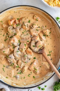A wooden spoon resting in a pan of Chicken Stroganoff.