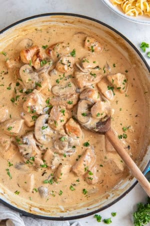 A wooden spoon resting in a pan of Chicken Stroganoff.