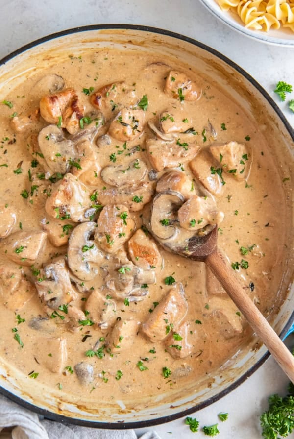A wooden spoon resting in a pan of Chicken Stroganoff.