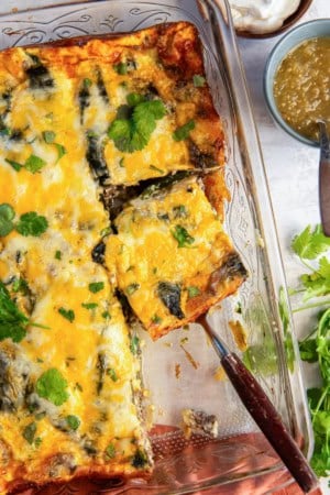 A spatula resting under a slice of chile relleno casserole in a baking dish.