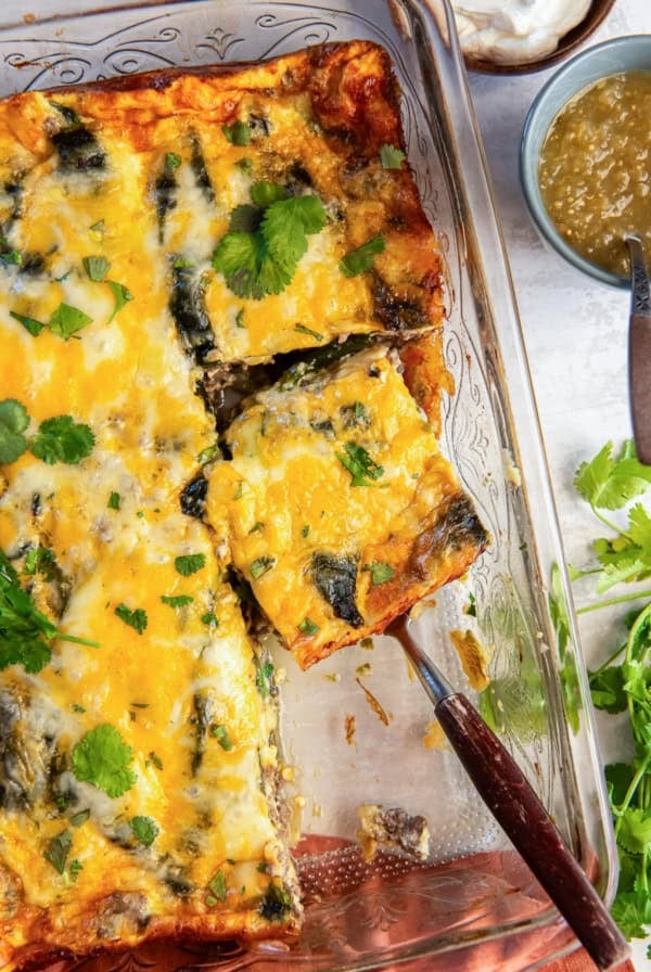 A spatula resting under a slice of chile relleno casserole in a baking dish.