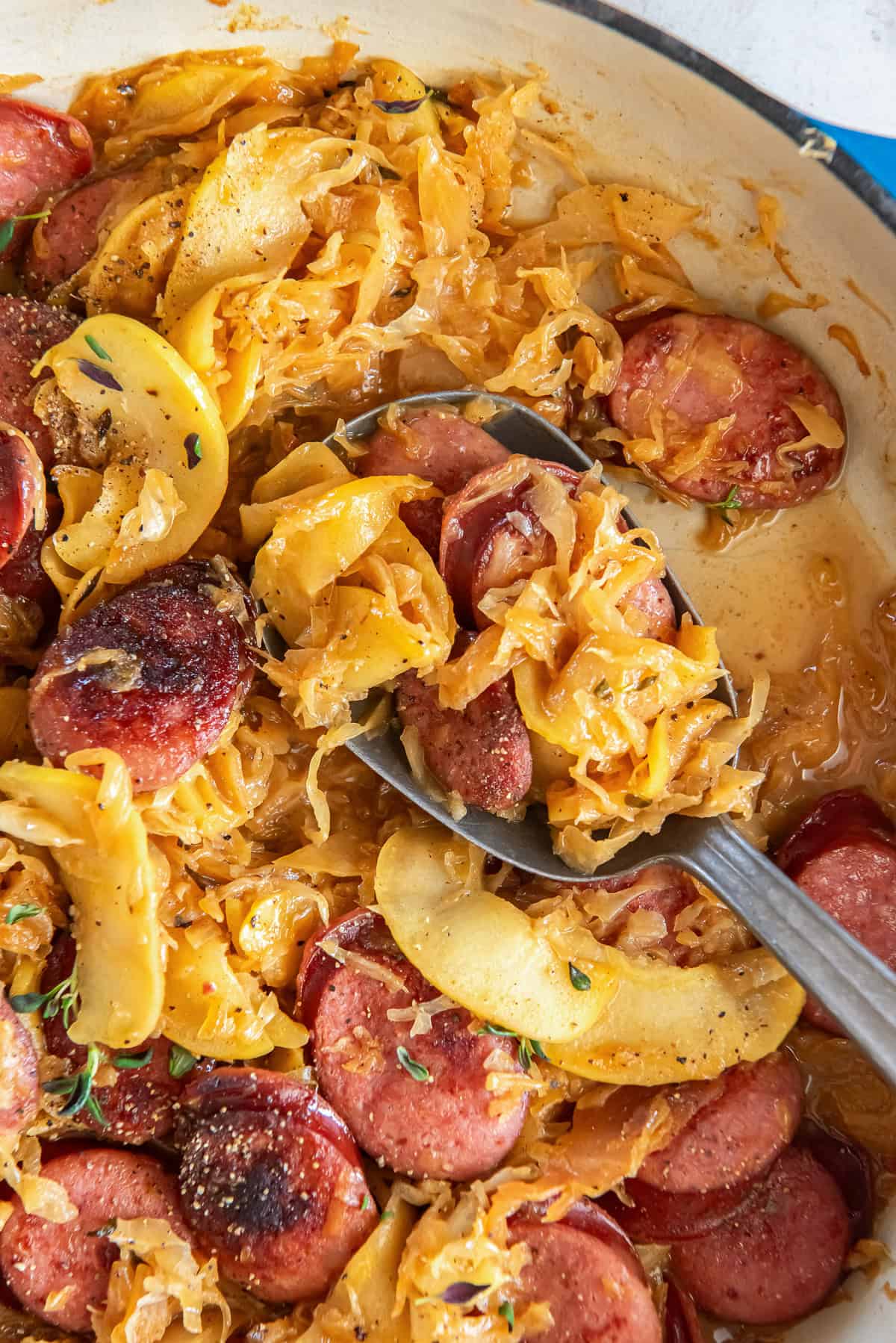 A spoon scooping kielbasa and sauerkraut from a skillet.