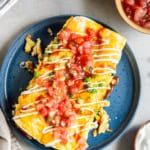 Two ham and cheese breakfast enchiladas on a blue plate with a fork.