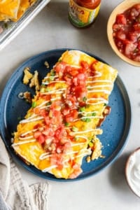 Two ham and cheese breakfast enchiladas on a blue plate with a fork.