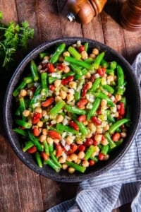 A black serving bowl filled with three bean salad next to a blue kitchen cloth.