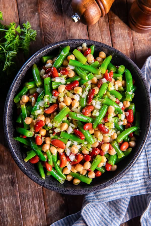 A black serving bowl filled with three bean salad next to a blue kitchen cloth.