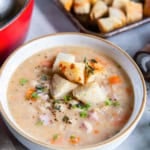 A bowl of white bean and ham soup topped with croutons next to a pot of soup and more croutons on a baking sheet.
