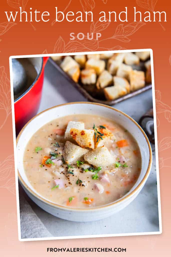 A bowl of white bean and ham soup topped with croutons and fresh thyme leaves with text overlay.