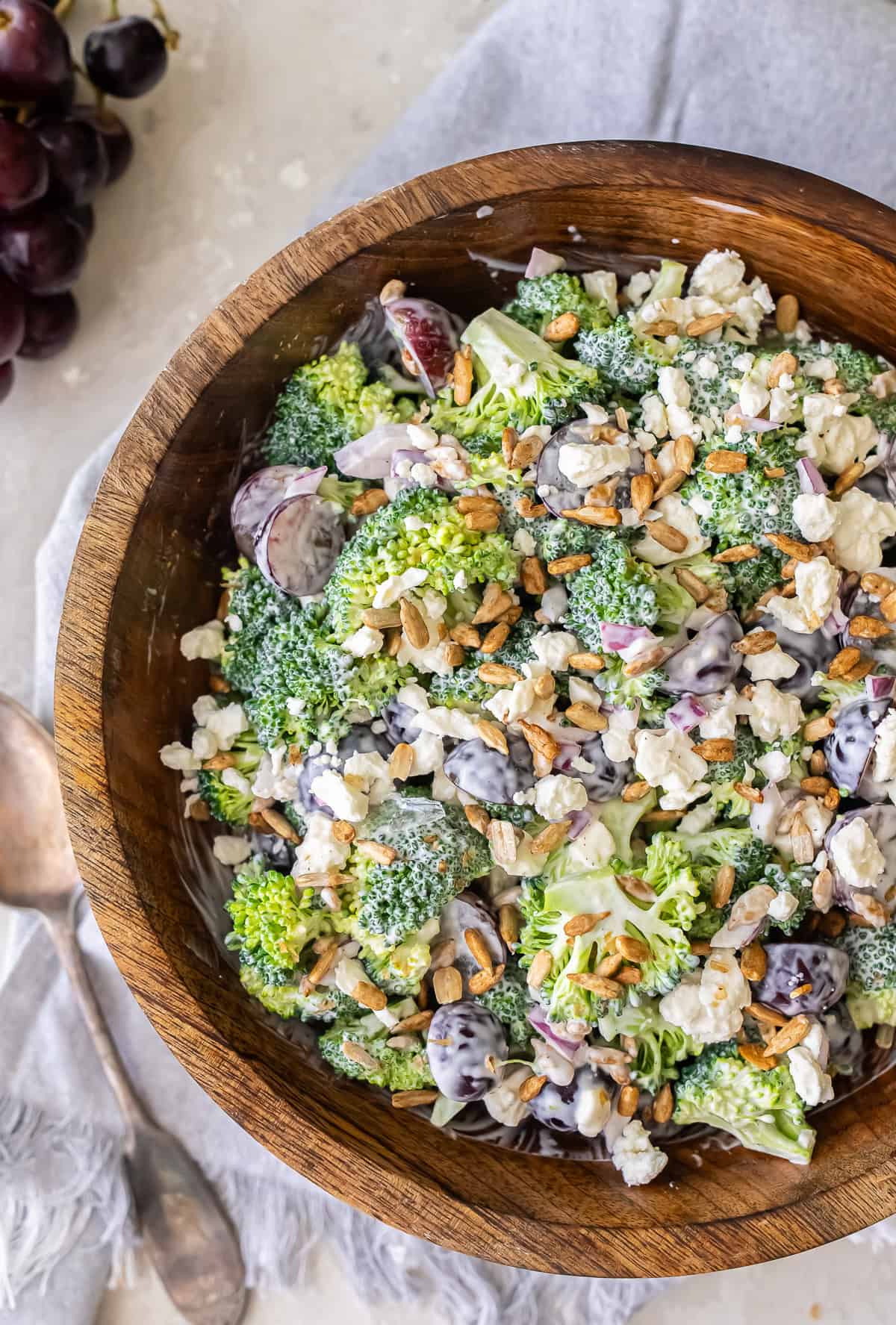 A serving spoon lying next to a wood bowl filled with broccoli grape salad.